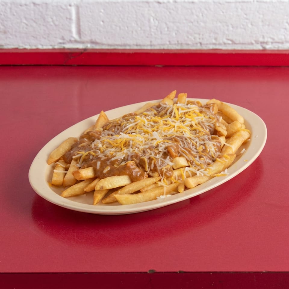Plate of golden fries covered in brown gravy and shredded cheese on a red diner table.